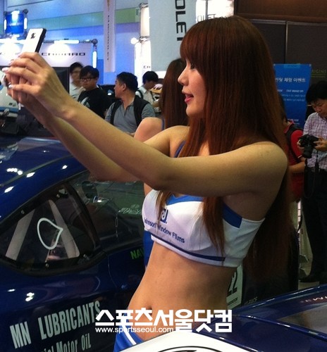 2012 서울오토살롱에서 한 레이싱걸이 관람객의 핸드폰에 사진을 직접 찍어주고 있다. / 황준성 기자.