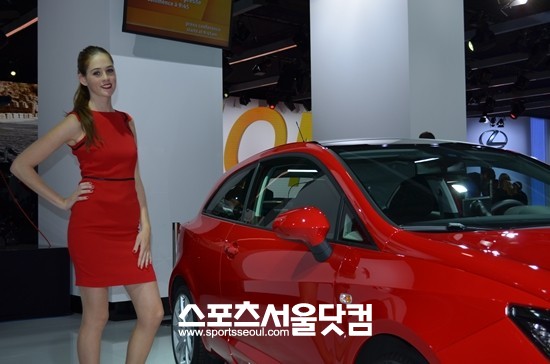 2012 파리모터쇼에서 빨간 원피스를 입은 한 모델이 빨간 자동차 옆에서 어색한 포즈를 취하고 있다.