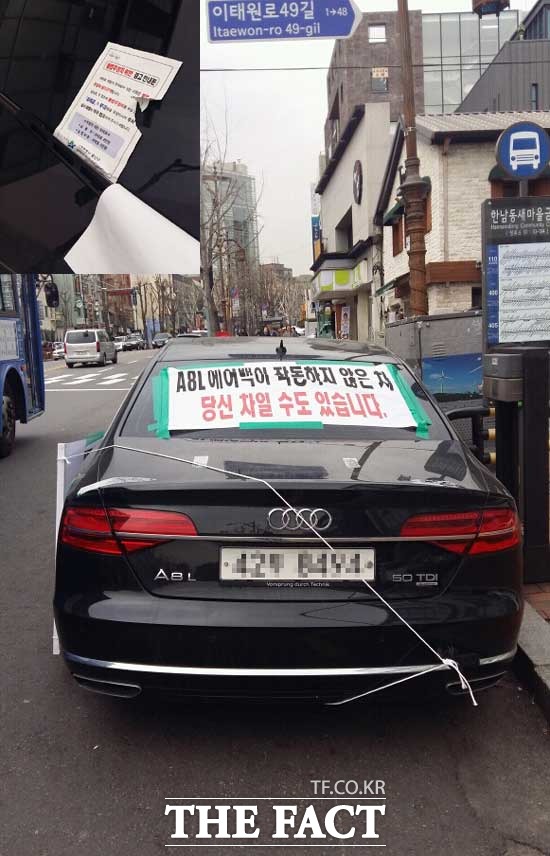 반파된 A8L 차량이 버스 정류장에 주차되어 있다. 차량의 전면 유리에 불법 주정차 위반 경고 안내문 2건이 부착되어 있다.