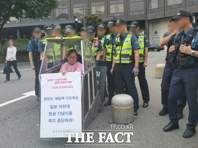 한 집회 참가자가 12일 서울 중구 밀레니엄 힐튼호텔 앞에서 경찰에 둘러 쌓인채 일본 자위대 62주년 창립 기념행사를 열지 마라는 피켓을 들고 있다.