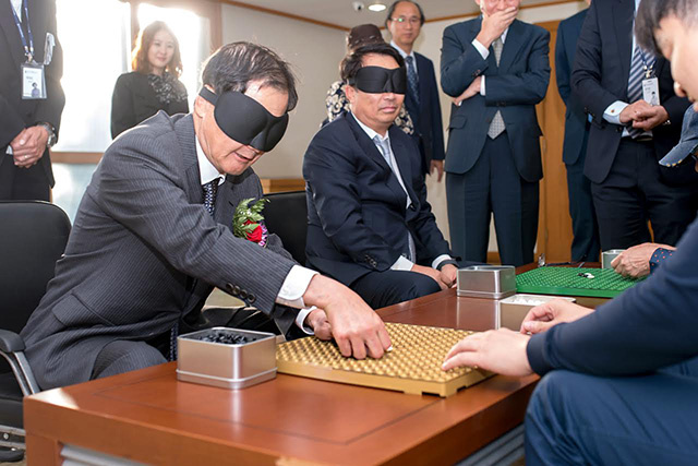 금호석유화학은 11일 서울시 강동구 소재 한국시각장애인복지관에 시각장애인용 흰지팡이 제작 후원금 5400만 원을 전달했다. 사진은 이날 박찬구 금호석유화학그룹 회장(왼쪽)이 안대를 착용하고 시각장애인 오목 경기를 직접 체험하고 있는 모습. /금호석유화학 제공