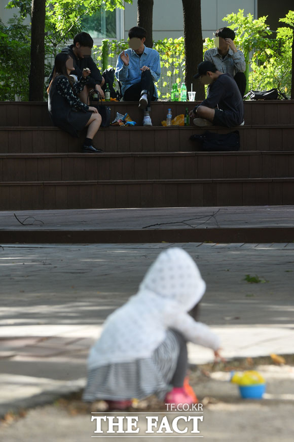 서울 마포구 상수동의 한 어린이 공원에서 소꿉놀이를 하는 어린이 너머로 청년들이 낮술을 즐기고 있다./최용민·남윤호 기자