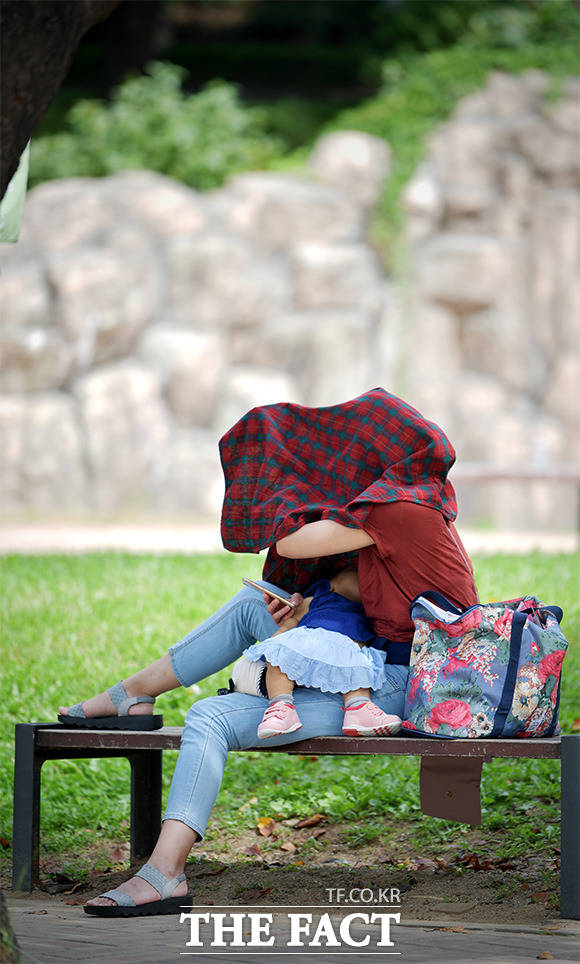 전국 대부분이 맑은 날씨를 보인 18일 오후 서울 광진구 능동로 어린이대공원을 찾은 한 아이의 엄마가 담요로 만든 그늘에서 아이를 재우고 있다. /이덕인 기자