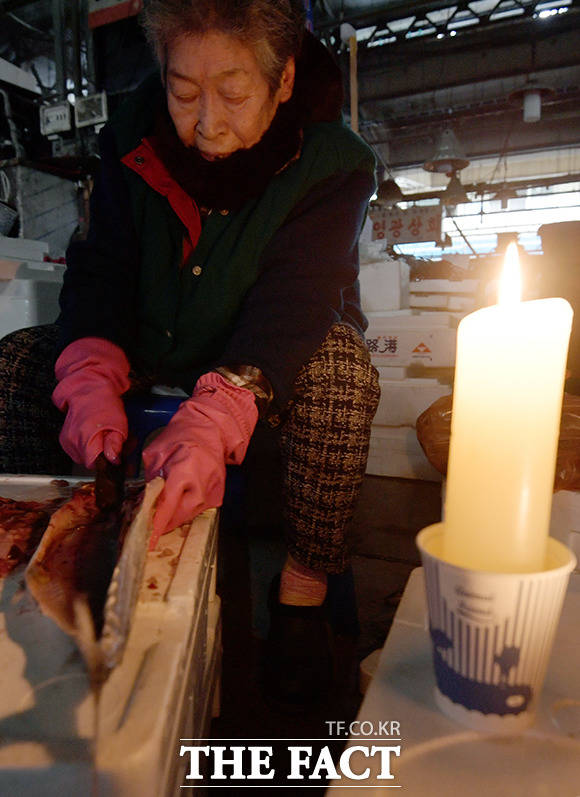 어두운 시장 한켠에서 촛불에 의지해 생선을 손질하는 할머니