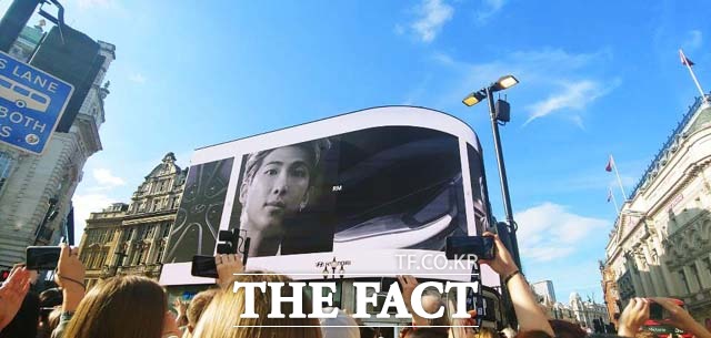 그룹 방탄소년단의 멤버 RM의 모습이 피카딜리 서커스 전광판에 나오고 있다. 방탄소년단 팬들은 이 모습을 담기 위해 일제히 휴대폰 카메라를 켜고 찍고 있다.