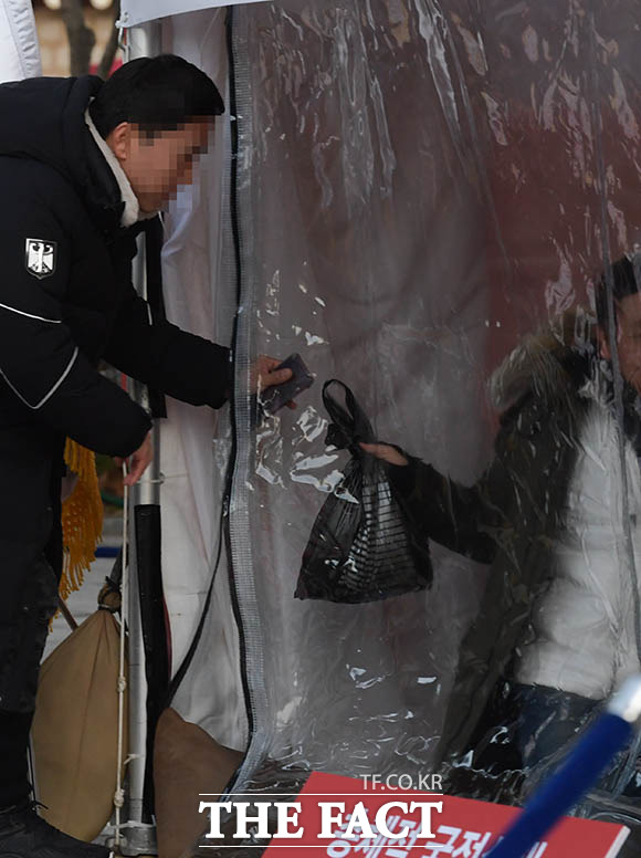 한 관계자가 천막 속으로 물건을 전달하고 있다.