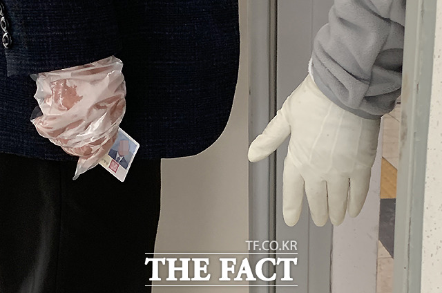 비닐장갑을 끼고 신분증을 들고 선 유권자와 안내하는 선관위 관계자의 위생장갑 낀 손이 나란히 보이고 있다.