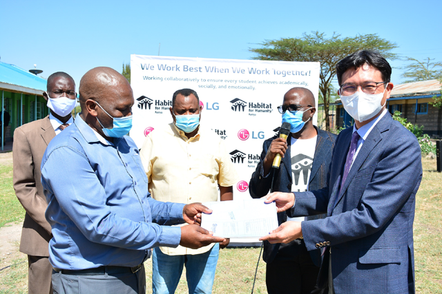 김사녕 LG전자 케나법인장(오른쪽)이 케냐 마차코스에 있는 쿰비 초등학교에서 쿰비 초등학교 이사회 알바나스 회장에게 희망마을 사업을 위한 건축 도면을 전달하고 있다. /LG전자 제공