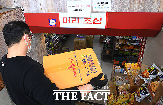 서울 건대 인근 과자할인마트에서 점주가 판매 상품을 나르는 가운데, 그의 머리 위로 24시 영업 시간이 표시된 안내문이 보이고 있다.