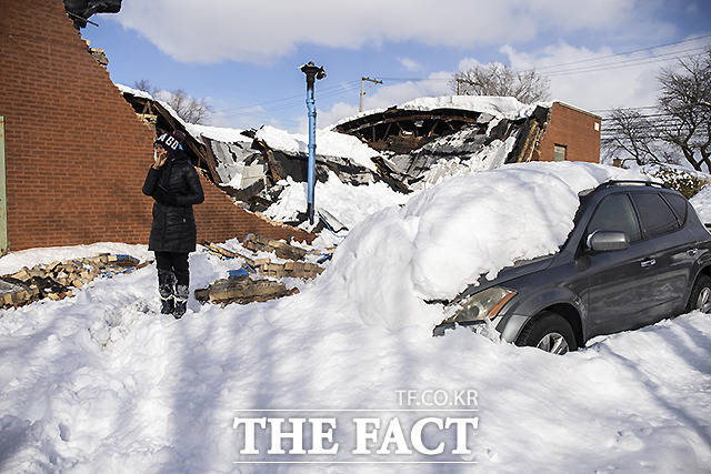 16일 전날 내린 폭설로 시카고 브레인어드 근교 세인트루이스의 건물이 붕괴된 가운데, 차주가 파손된 차 옆에 서 있다.