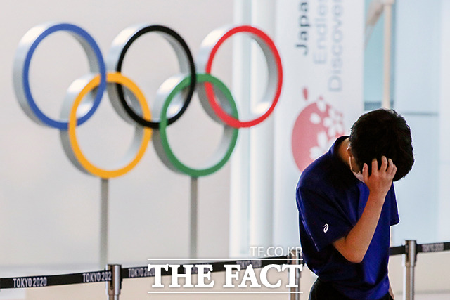 8일 일본 도쿄 하네다 공항에 설치된 올림픽 오륜기 광고판 앞에서 공항직원이 고개를 숙이고 있다. /도쿄=로이터