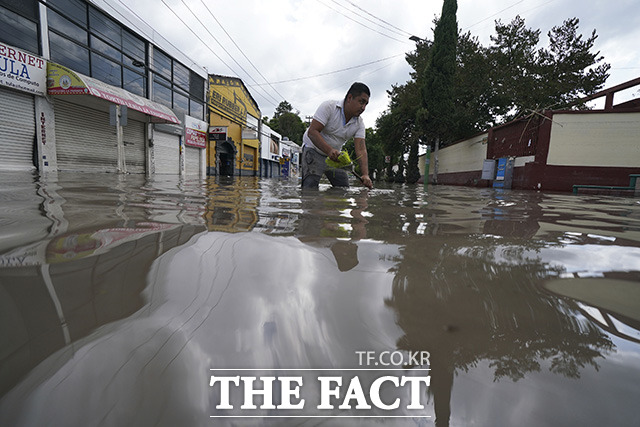 침수된 거리의 물을 빼내기 위해 맨홀 뚜껑을 열고 있는 한 남성.