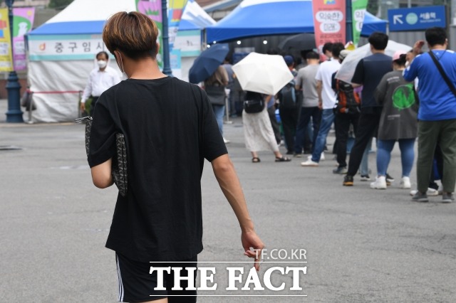 한 남성이 서울역 인근에서 담배를 들고 걸어가고 있다. 이 남성 옆으로는 코로나19 검사를 기다리는 시민들이 줄을 서 있다. /남윤호 기자