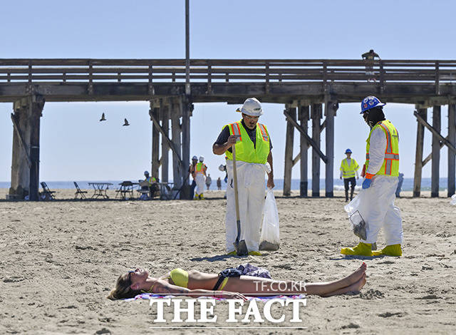 미 캘리포니아주 뉴포트비치 부두 남쪽 해변에서 발생한 기름유출 사고로 관계자들이 기름 제거 작업을 벌이고 있는 5일(현지시간) 한 여성이 해변에 누워 일광욕을 하고 있다./헌팅턴비치=AP.뉴시스