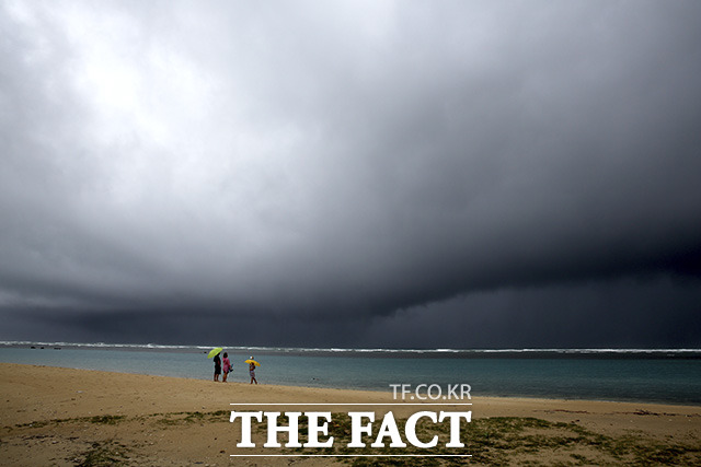 6일(현지시간) 미 하와이주 호놀룰루의 한 텅 빈 해변에 짙은 먹구름이 드리운 가운데 비가 내리기 시작하자 사람들이 우산을 쓰고 있다. /호놀룰루=AP.뉴시스