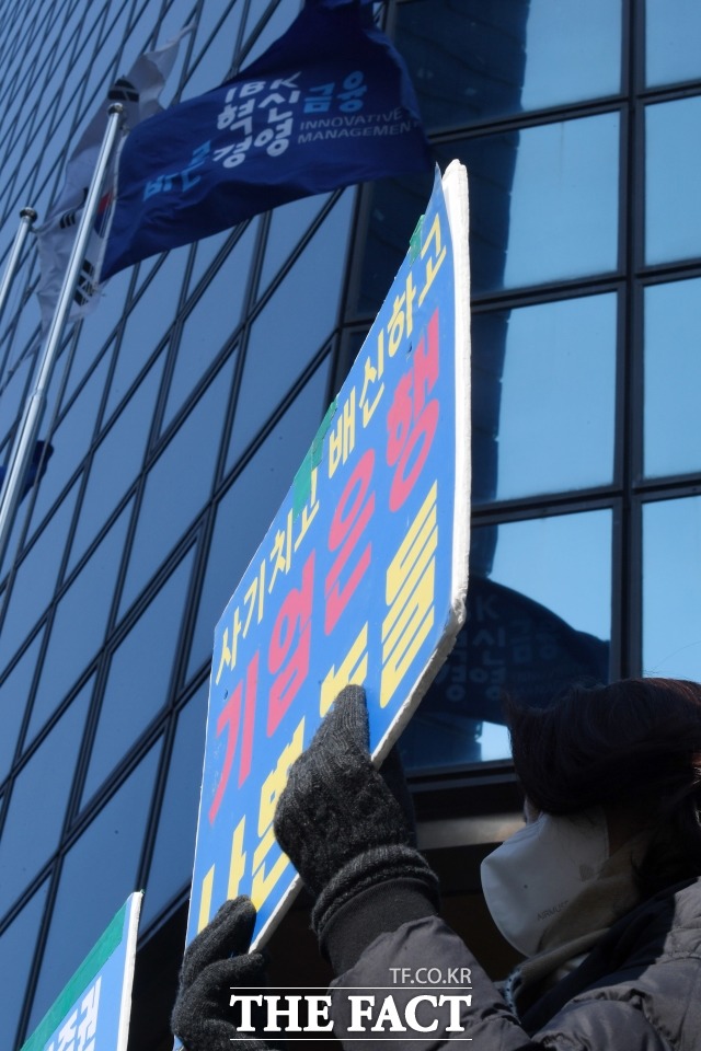 디스커버리펀드 진실규명을 위한 피해자들의 기자회견이 16일 오전 서울 을지로 기업은행 본사 앞에서 열린 가운데 손피켓을 들어보이는 피해자 위로 기업은행 사기가 바람에 휘날리고 있다./남용희 기자