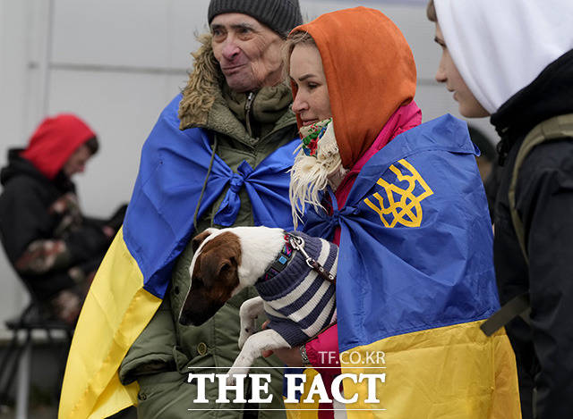 우크라이나 국기를 몸에 두른 남녀가 8일(현지시간) 반려견을 안고 폴란드 프셰미실의 난민 쉼터에 들어서고 있다. /프셰미실=AP.뉴시스