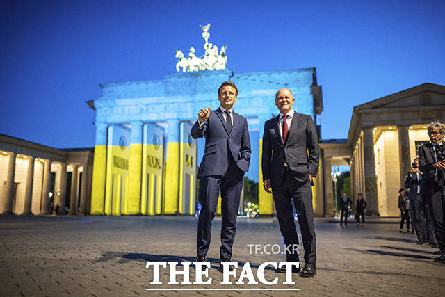 독일을 방문한 에마뉘엘 마크롱(왼쪽) 프랑스 대통령이 9일(현지시간) 우크라이나 국기 색상 조명으로 물든 베를린 브란덴부르크문 앞에서 올라프 숄츠 독일 총리와 함께 포즈를 취하고 있다. /베를린=AP.뉴시스