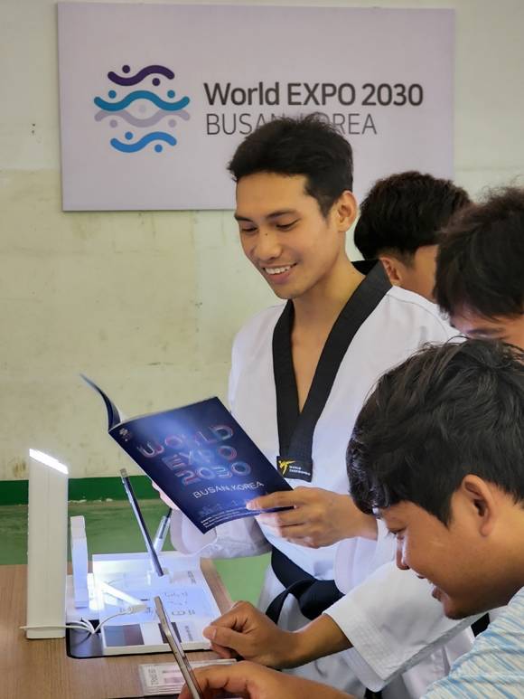 태권도대회에 참가한 캄보디아 청소년 선수들이 스마트폰, TV 등 삼성전자 제품을 체험하고 부산엑스포 안내 책자를 살펴보고 있다. /삼성전자 제공