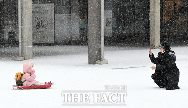 서울을 비롯한 수도권 대부분 지역에 대설주의보가 발효된 21일 오전 경기도 수원 장안구의 한 엄마와 아이가 눈썰매를 타고 유치원으로 향하는 중 기념 사진을 찍고 있다./수원=임영무 기자