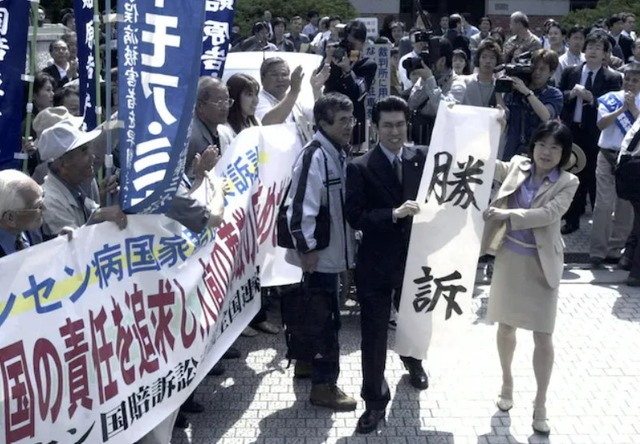 2001년 5월 구마모토 판결 승소 현수막을 펴든 사코다 도키코 변호사(오른쪽). 소록도를 다시 찾은 그는 건배사에서 딸이 한국 걸그룹 르세라핌을 좋아한다며 어떻게든 사람들은 다 이어질 수 있다고 말했다. /일본교도통신 갈무리
