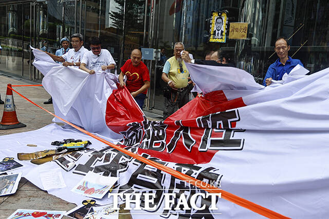 24일 홍콩 중심가에서 일본의 후쿠시마 원전 오염수 해양 방류에 항의하는 시위대가 세계의 적이라고 쓰인 대형 일본 국기를 찢고 있다. 일본 수산물의 최대 수입국인 홍콩은 일본의 후쿠시마 원전 오염수 방류에 반대하면서 오늘부터 일본산 수산물의 수입을 금지한다고 발표했다. /홍콩=AP.뉴시스