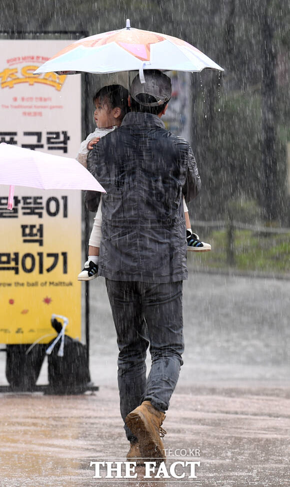 우산을 쓴 채 어린 딸을 안고 빗길을 걷는 남성의 어깨가 젖어 있다.