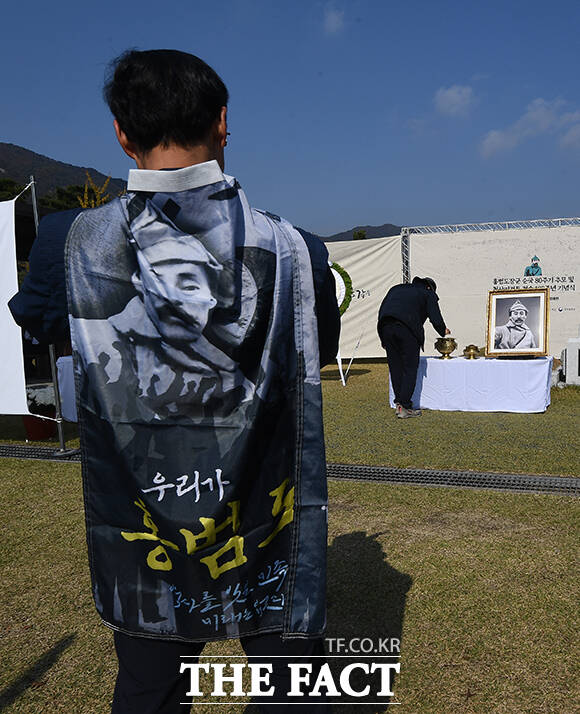 한 시민이 홍범도 장군의 그림이 그려져있는 옷을 걸치고 홍 장군의 묘역을 바라보고 있다.