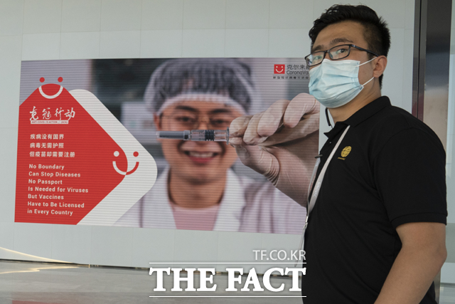 24일(현지시간) 중국 제약사 시노백의 베이징 공장에서 한 직원이 신종 코로나바이러스 감염증 광고판 앞에 서 있다. /베이징=AP.뉴시스
