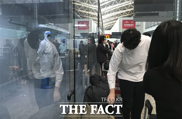 중국 정부는 코로나19 관련 사망자 급증에도 불구하고 내달 8일부터 해외발 입국자 시설 격리 조치를 폐지하기로 결정했다. 사진은 25일(현지시간) 중국 남부 광둥성 광저우 바이윈 국제공항에서 검역 시설로 출발하기 위해 대기하는 입국 여행자들과 유리 너머로 방호복을 입고 근무하는 공항 관계자의 모습. /광저우=AP.뉴시스