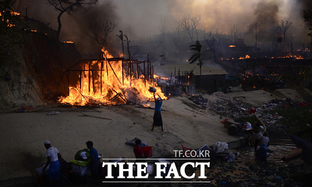 5일(현지시간) 방글라데시 콕스 바자르에 있는 로힝야족 난민캠프에 화재가 발생한 가운데 난민들이 가옥에 물을 뿌리며 불을 진압하고 있다. /콕스바자르=AP.뉴시스
