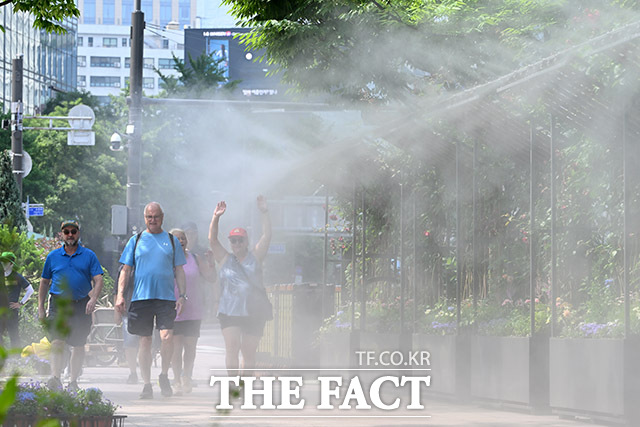 낮 최고기온이 30도 안팎의 무더위가 예고된 18일 오전 서울 중구 서울시청 앞 서울광장을 찾은 관광객들이 쿨링포그 앞을 지나가며 더위를 식히고 있다. /남용희 기자