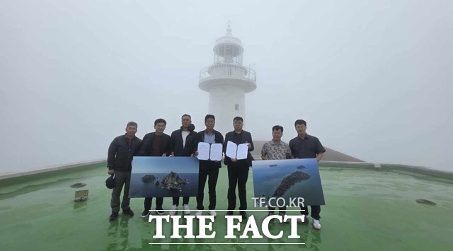 독도사랑운동본부 노상섭 회장(오른쪽) 일행과 격렬비열도사랑운동본부 윤현돈 회장(왼쪽) 일행 7명은 25일 장마 속 궂은 날씨에도 격렬비열도를 방문해 격렬비열도 등대를 배경으로 이날 체결한 업무협약서를 들고 기념촬영을 하고 있다. /격렬비열도사랑운동본부.