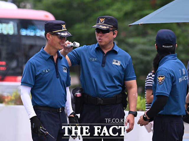 전국 대부분 지역에 폭염특보가 내려진 8일 오후 서울 광화문 일대에서 야외 근무 중인 경찰관이 동료에게 휴대용 선풍기를 쐬어주고 있다.