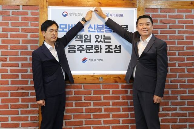 지난 14일 서울 서초동 하이트진로 본사 인근 착한가격업소에서 김인규 하이트진로 대표(오른쪽)와 김민재 행정안전부 차관(왼쪽)이 모바일 신분증 활용을 권장하는 홍보 포스터를 부착하고 있다. /하이트진로