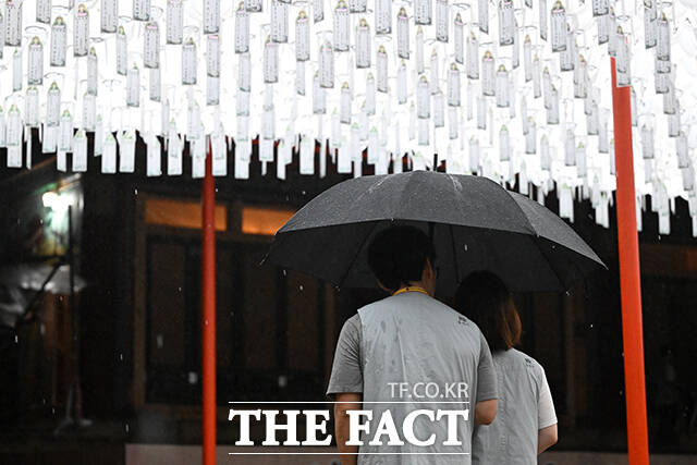 야간 데이트를 하는 참가자들이 함께 우산을 쓰고 연등 아래를 걷고 있다.