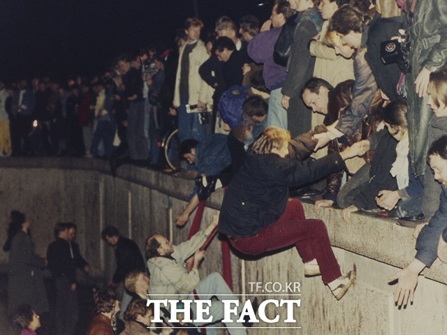 2025년 10월 3일로 독일은 통일 35주년을 맞았지만, 한반도는 여전히 분단된 상태다. 전문가들은 대북 정책의 일관성이 무엇보다 중요하다고 제언했다. 사진은 지난 1989년 11월 10일 동독 동베를린 브란덴부르크 문 근처에서 주민들이 베를린 장벽을 오르며 서독 서베를린 주민들의 도움을 받는 모습. /AP.뉴시스