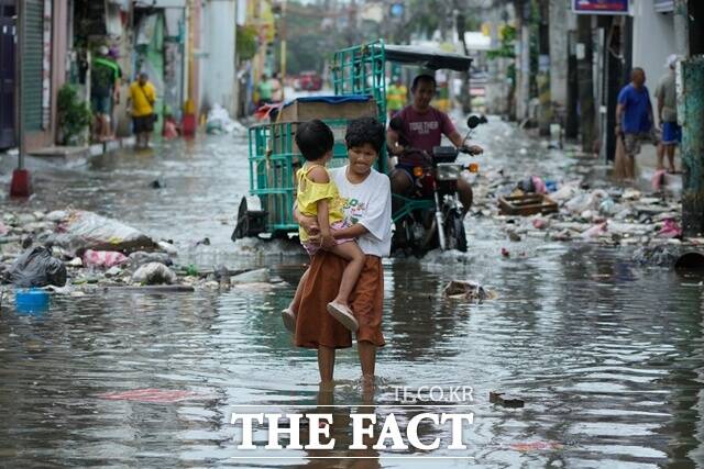 지난 10일(현지시간) 필리핀 해안 마을 나보타스에서 아이를 안은 한 주민이 태풍 풍웡과 만조로 침수된 거리를 건너고 있다. /뉴시스