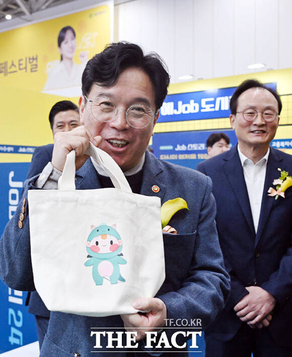 김영훈 고용노동부 장관이 19일 대전컨벤션센터 제2전시장에서 열린 고용노동부와 함께하는 청년의 내일(My Job), 2025 KB굿잡 대전 일자리 페스티벌에 참석해 고용노동부가 운영하는 Job 스토리24 부스를 참관한 뒤 고용노동부 캐릭터 고드래곤이 그려진 에코백을 들어보이고 있다. 오른쪽은 이환주 KB국민은행장.