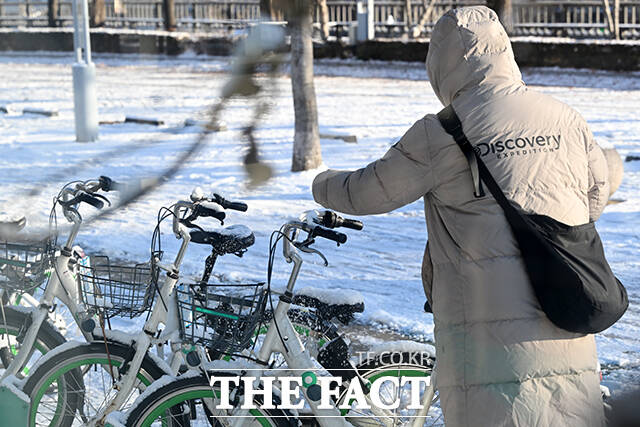 한 시민이 따릉이에 쌓인 눈을 털고 있다.
