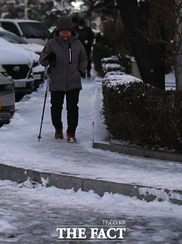 한 주민이 등산 스틱을 짚으며 눈이 얼어붙은 빙판길을 걷고 있다.