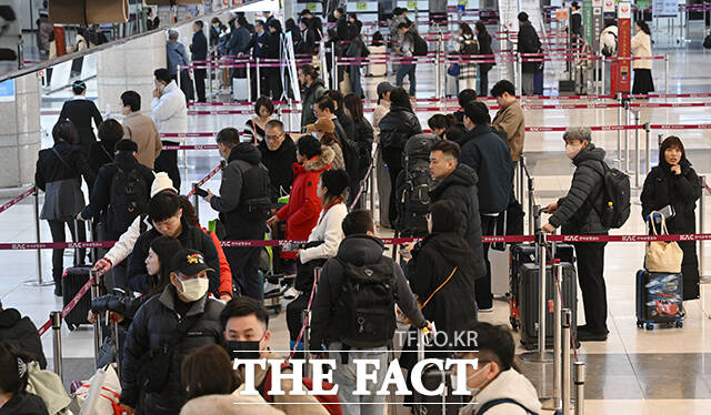 두꺼운 외투를 입은 관광객들이 수하물을 부치기 위해 기다리고 있다.