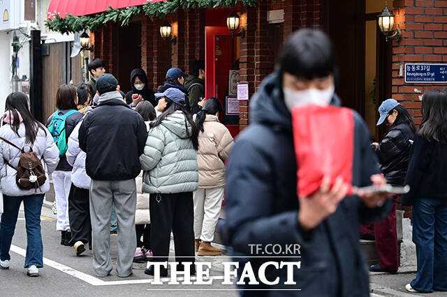 두쫀쿠를 바라보며 걸음 옮기는 시민 뒤로 줄이 여전히 늘어서 있다.