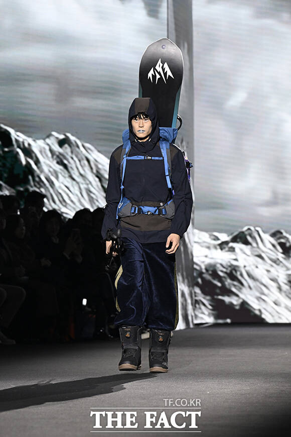모델이 스노보드를 등에 진 채 런웨이를 걷고 있다.