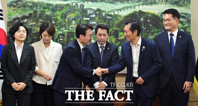 김민석(왼쪽 세번째)·정청래 더불어민주당 당대표 예비후보가 악수를 하는 가운데, 사이에 자리한 임만균 서울시의회 의장이 어색한 표정을 짓고 있다.