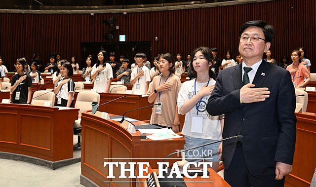 최교진 교육부 장관(오른쪽)과 어린이 국회의원들이 예결위원회 회의장에서 국기에 경례하고 있다.