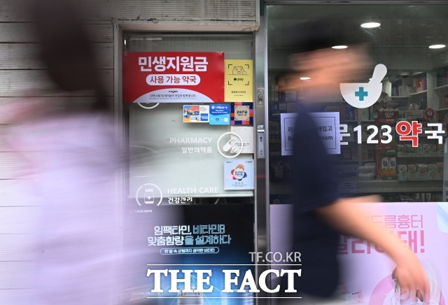 2025년 7월 21일 시민들이 서울 종로구의 한 약국 앞을 지나가고 있다. 에 민생회복소비쿠폰 사용처 안내문이 붙어 있다. /이새롬 기자