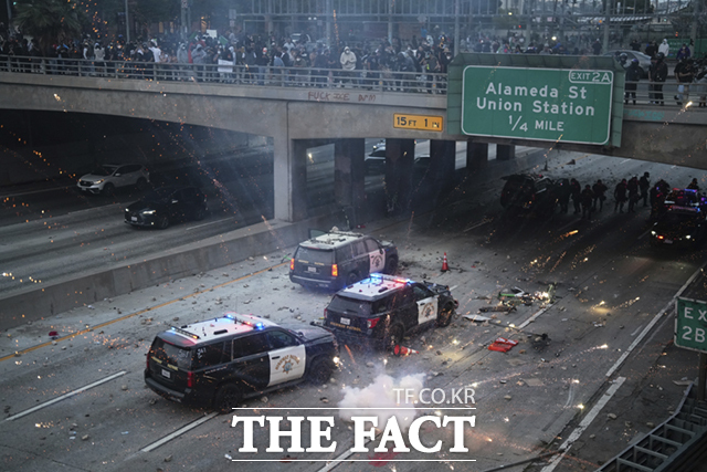 8일(현지시간) 미 캘리포니아주 로스앤젤레스 도심 메트로폴리탄 구치소 인근 101번 고속도로에서 이민세관단속국(ICE)의 불법 이민자 단속 및 체포에 항의하는 시위대가 경찰차를 향해 돌을 던지고 섬광탄을 터트리고 있다. /로스엔젤레스=AP.뉴시스